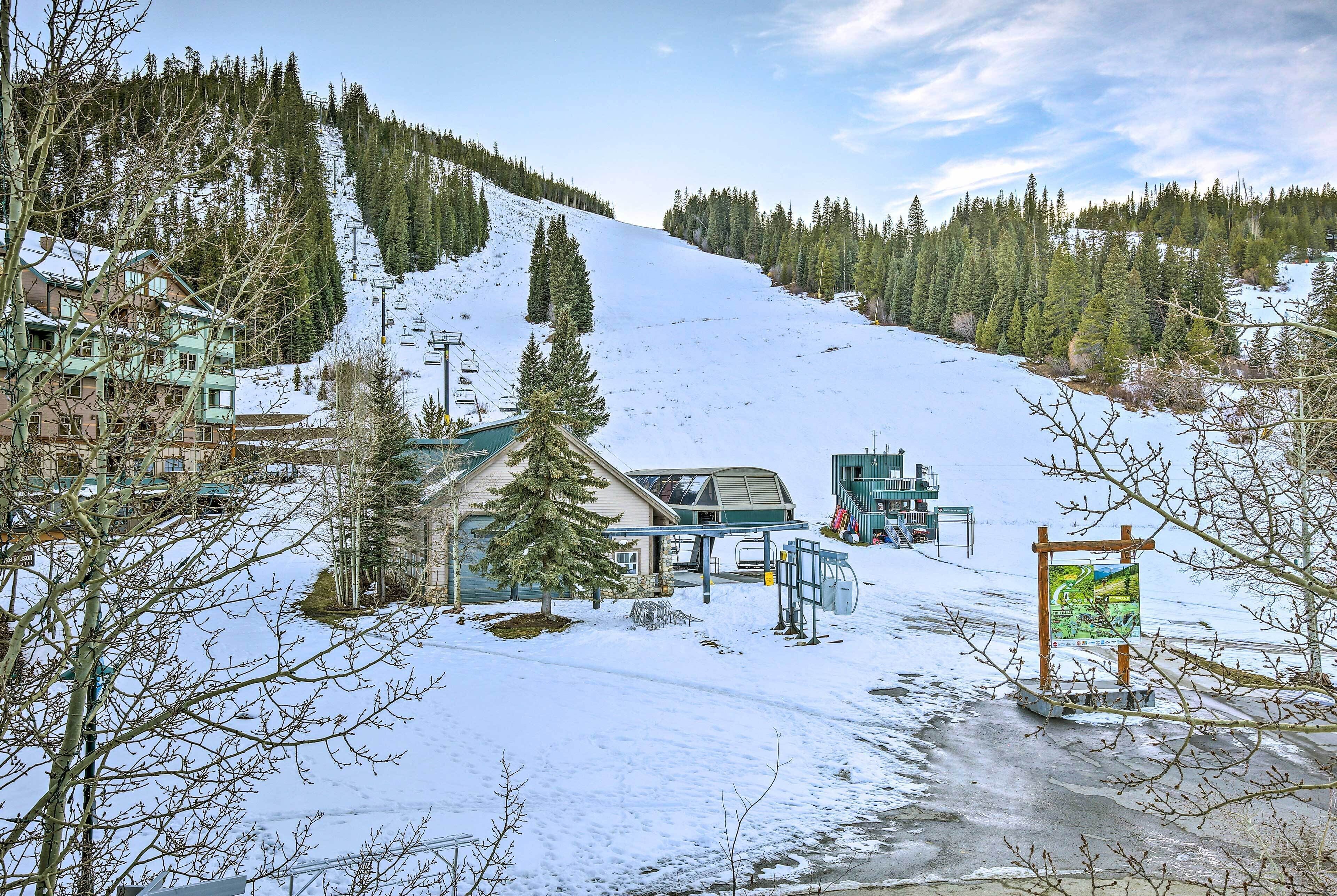 A ski resort with a chairlift, snow-covered slopes, and buildings with a mountain backdrop.