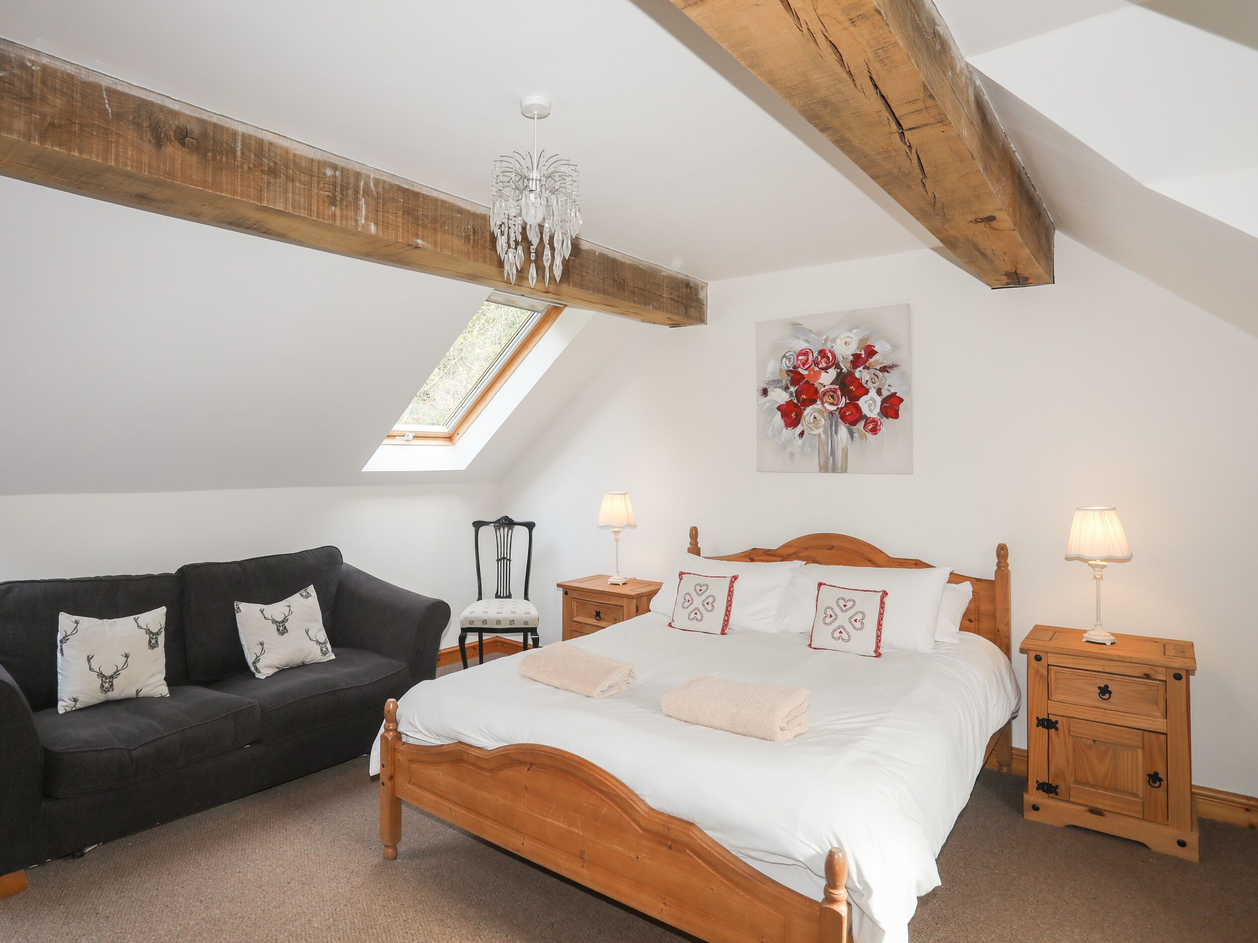 Une chambre avec un plafond en pente, un cadre de lit en bois, un canapé foncé et une table de chevet avec une lampe.