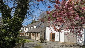 Une maison de campagne traditionnelle en pierre, avec une porte en bois, une allée gravillonnée et une clôture en bois.