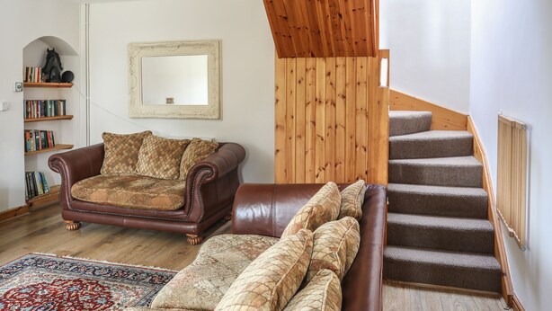 Un salon avec un canapé en cuir marron, un tapis à motifs, un escalier en bois et une bibliothèque contenant des livres et une figurine de cheval.