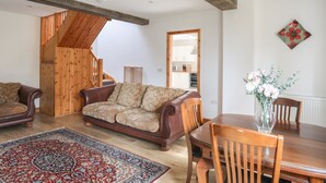 Un vaste salon doté d’un canapé en cuir marron, d’un tapis à motifs, d’une table à manger en bois et de chaises. Un escalier en bois mène à l’étage supérieur.