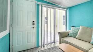 A room with teal walls, a white door, a beige sofa with patterned cushions, and a wooden bench. - Remodeled Siesta Key Studio Near Beach! (Siesta Key)