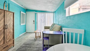 A room with teal walls, a herringbone-patterned wooden cabinet, a beige sofa, a small round table, and a white chair. - Remodeled Siesta Key Studio Near Beach! (Siesta Key)