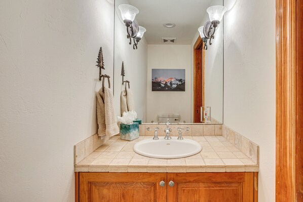 A bathroom with a white sink, wooden cabinets, and two wall-mounted light fixtures. - Luxurious Ski-in/ski-out Telluride Mountain Escape (Telluride)
