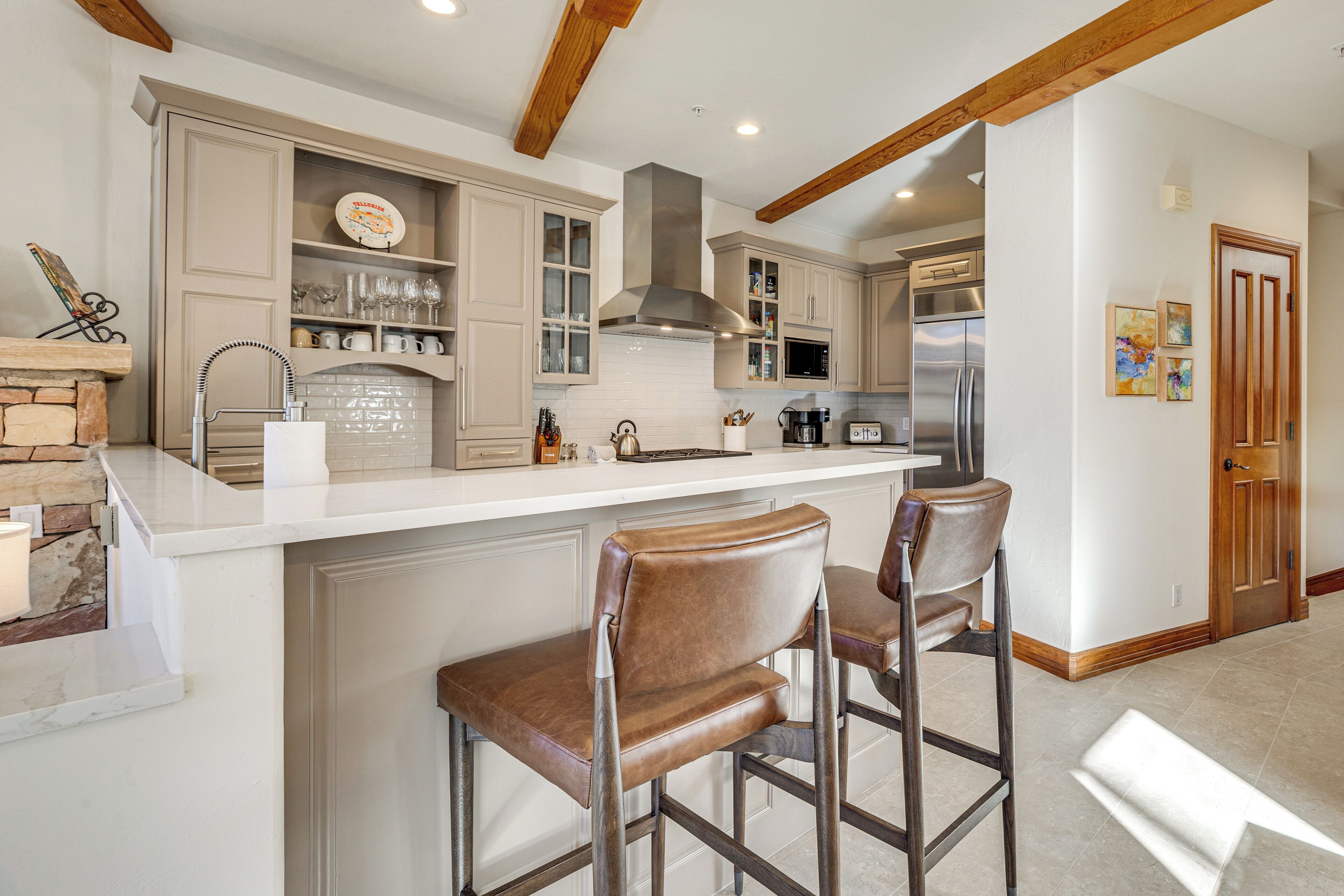 A kitchen with a white countertop, stainless steel appliances, and wooden bar stools.