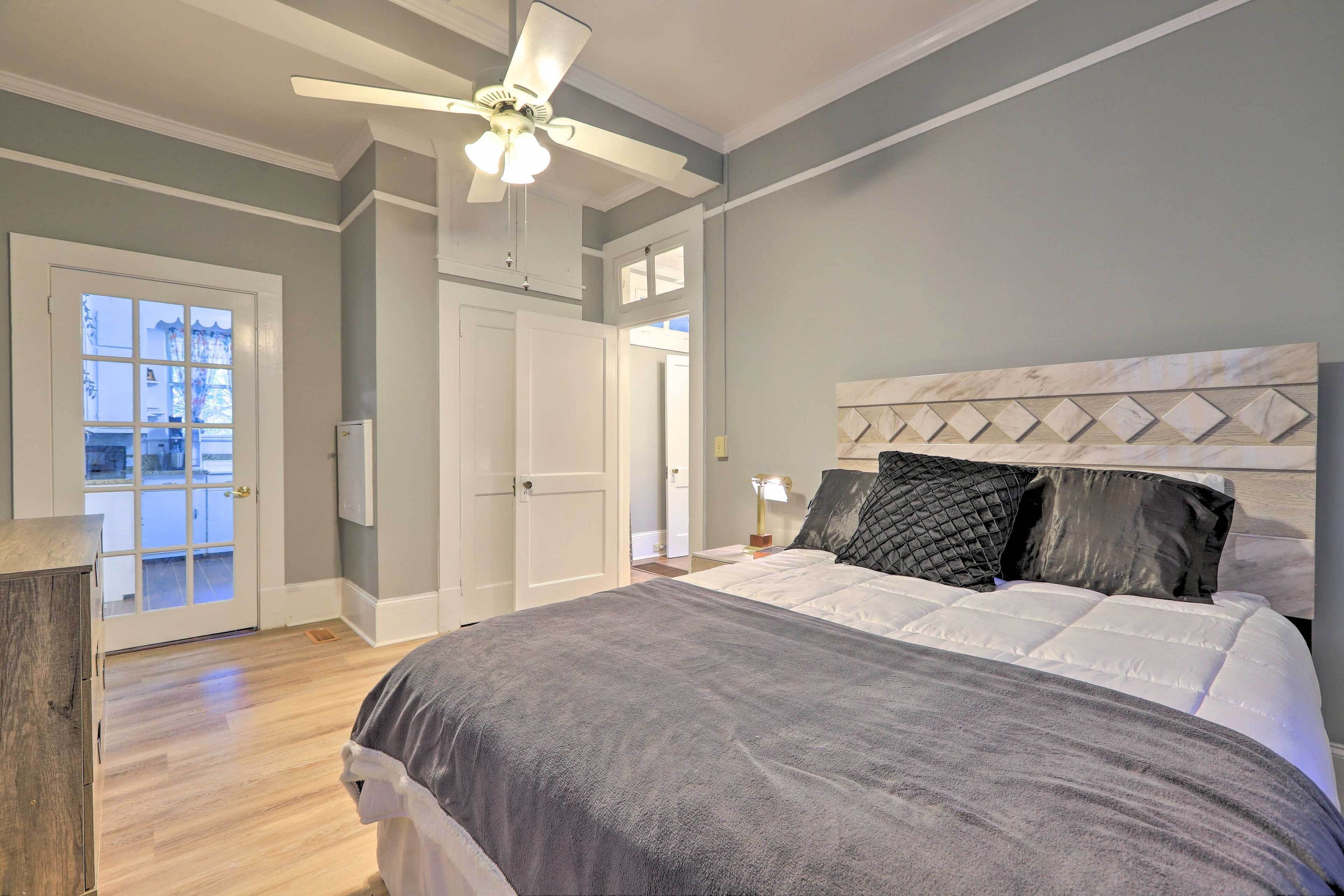A bedroom with a bed, a ceiling fan, a door, and a view through a window.