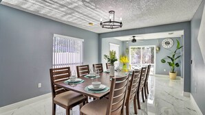 A dining area with a table set for six, chairs, a chandelier, and a clock on the wall. - Modern Clearwater Home w/ Deck: 9 Mi to Beach (Clearwater)