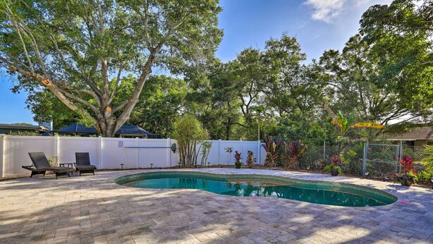A swimming pool with a herringbone tile pattern, surrounded by trees and a white fence. - Modern Clearwater Home w/ Deck: 9 Mi to Beach (Clearwater)