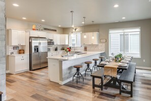 A modern kitchen with white cabinets, a large island with stools, a built-in refrigerator, and pendant lighting. - Spacious, Rustic Spearfish Home: Walk to Downtown! (Spearfish)