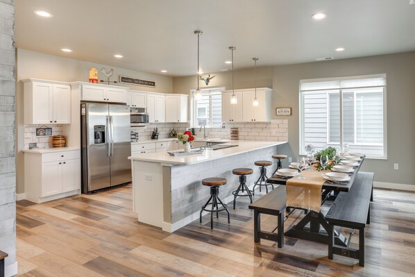 A modern kitchen with white cabinets, a large island with stools, a built-in refrigerator, and pendant lighting.