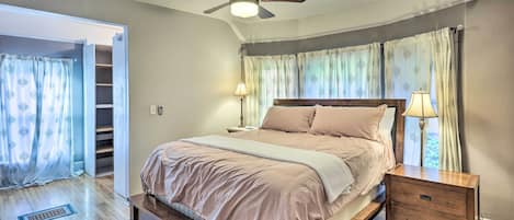 A bedroom with a bed, a nightstand, a ceiling fan, and a window with curtains.