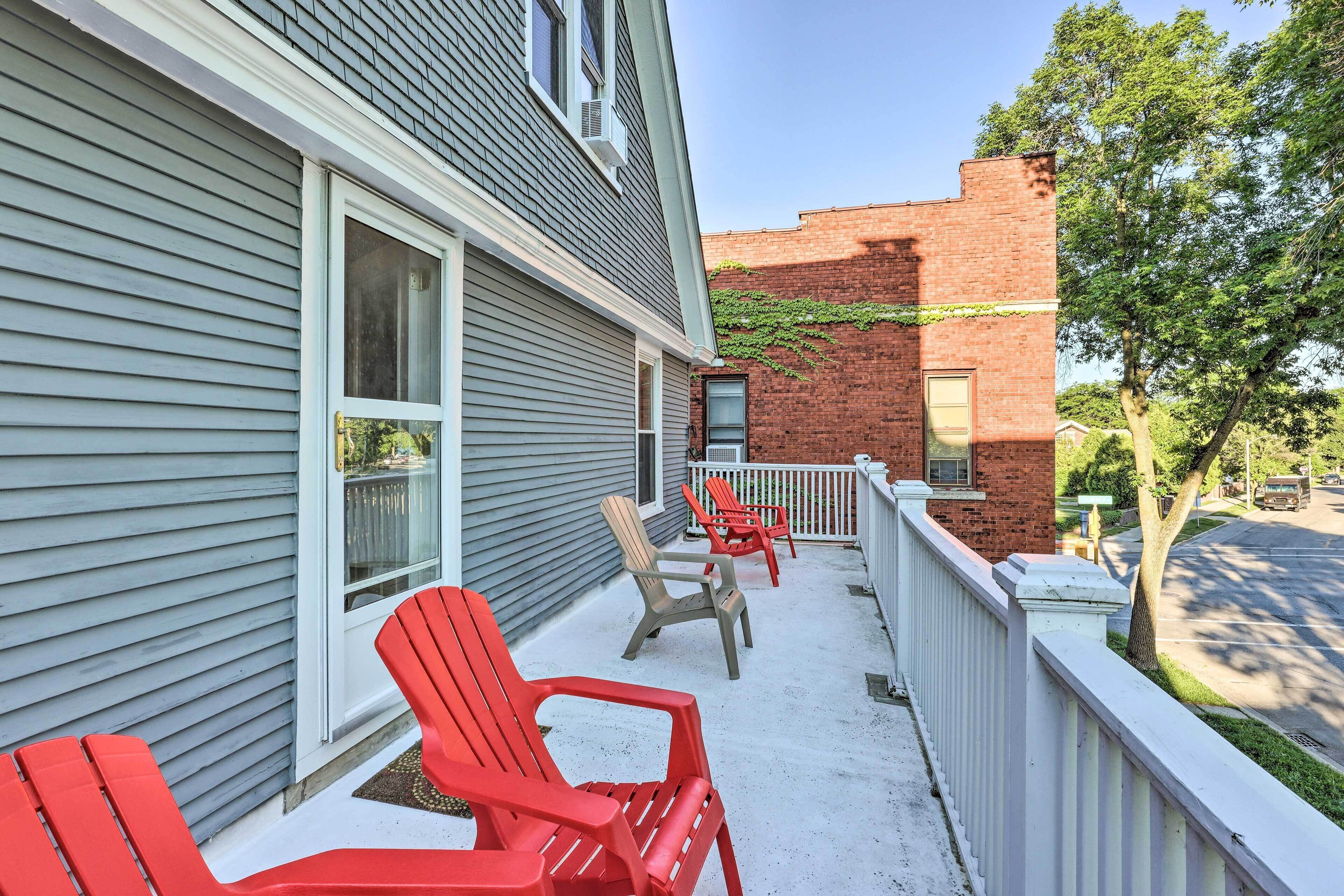 Une véranda avec des fauteuils Adirondack rouges, un bâtiment en briques et une clôture blanche.