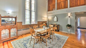 A dining area with a wooden table and chairs, a large window with stained glass, and a view of the upper floor. - Lisle Apt: Fireplace & Stained Glass Windows! (Lisle)