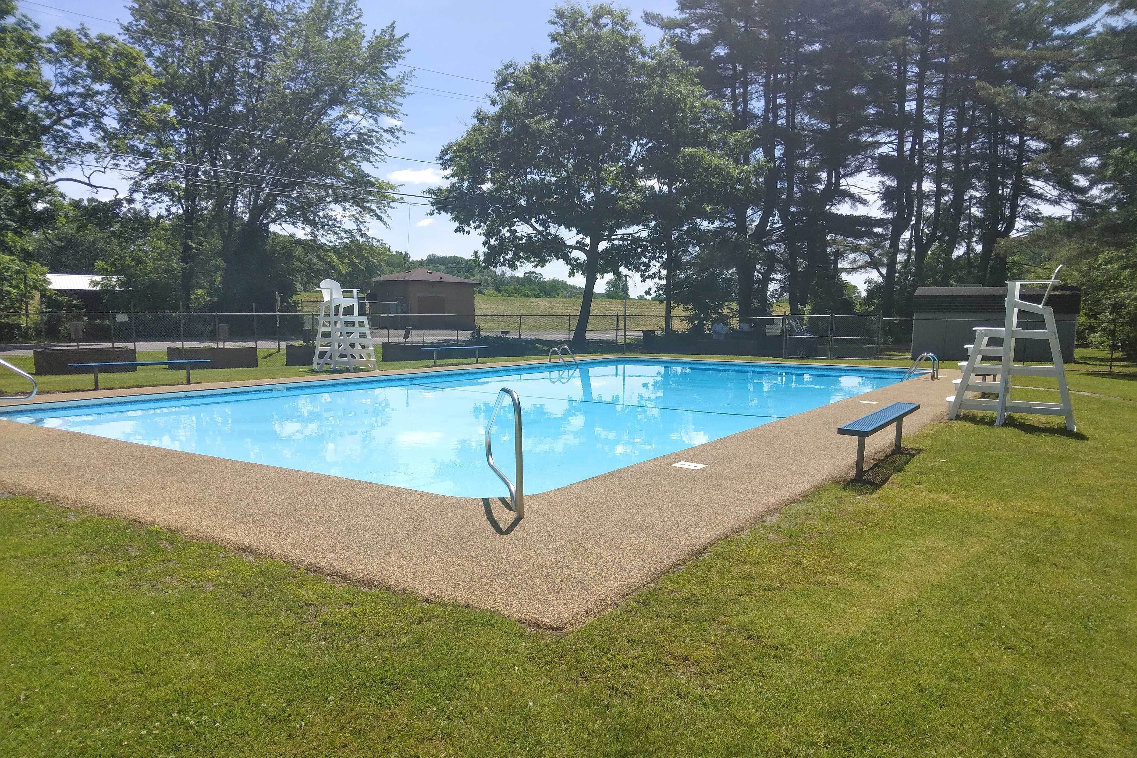 A rectangular swimming pool with a ladder and a lifeguard stand, surrounded by grass and trees.