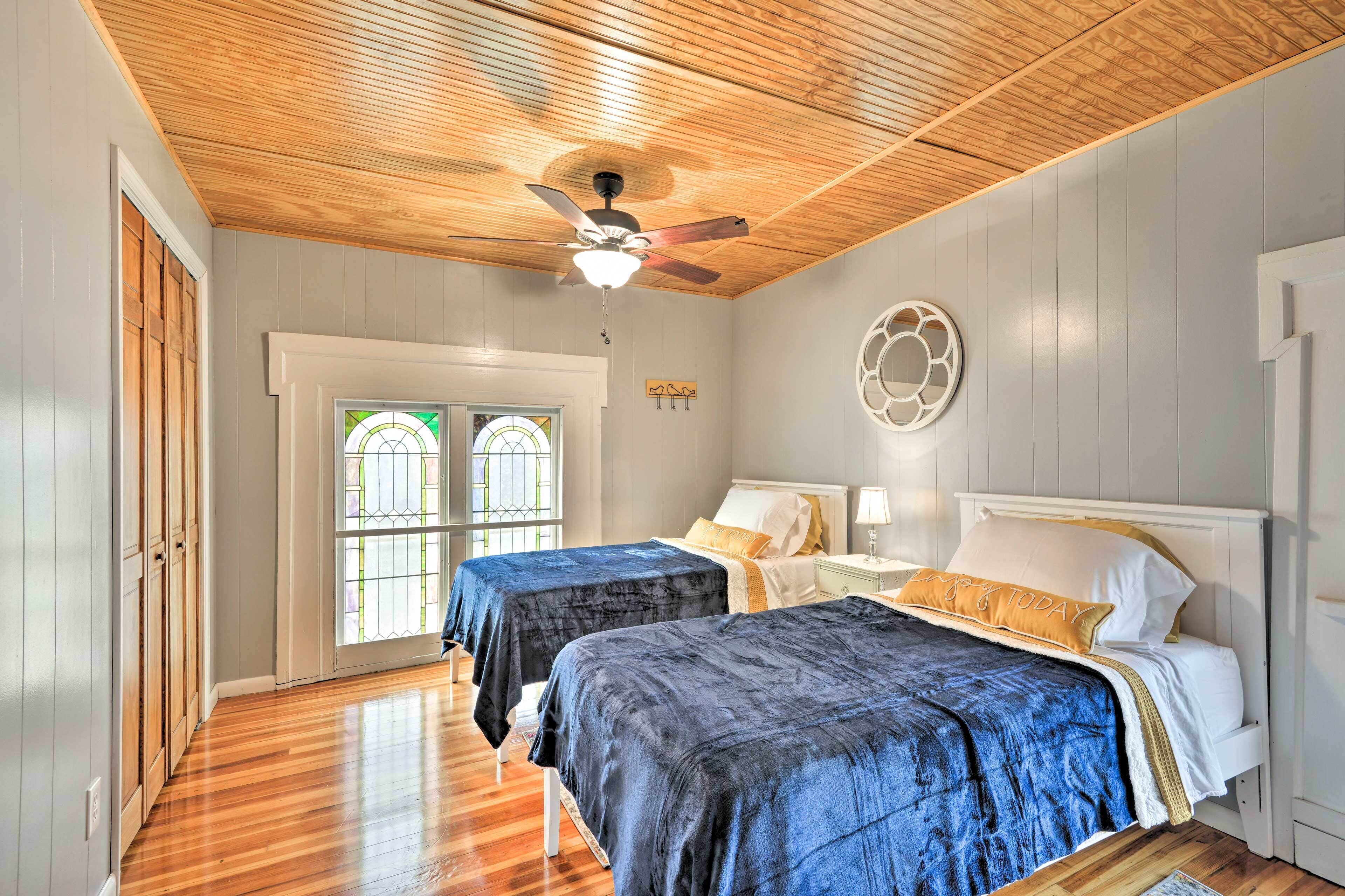 A room with two beds, wooden flooring, a ceiling fan, and a window with a view.