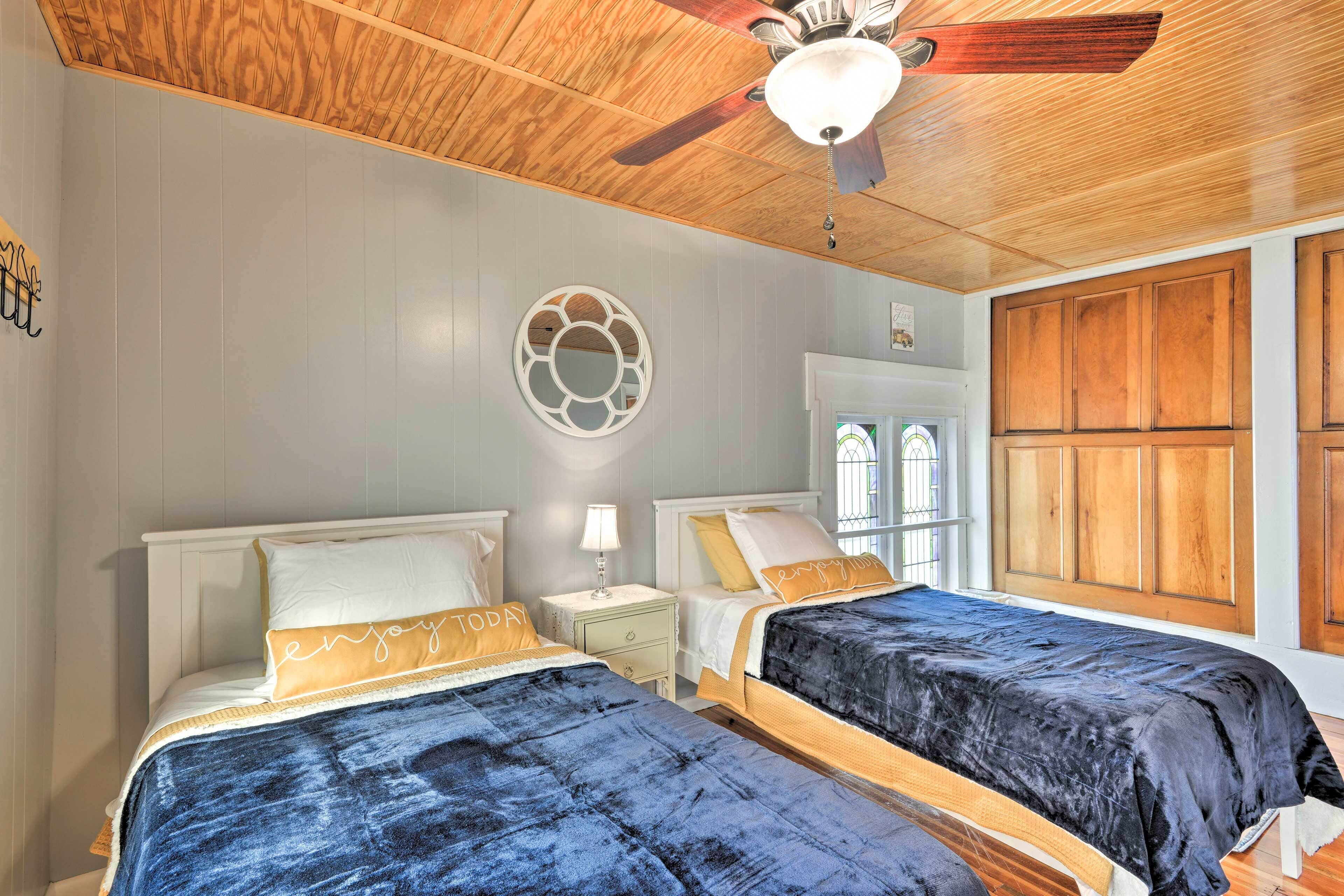 A bedroom with two beds, a ceiling fan, and a decorative wall piece.