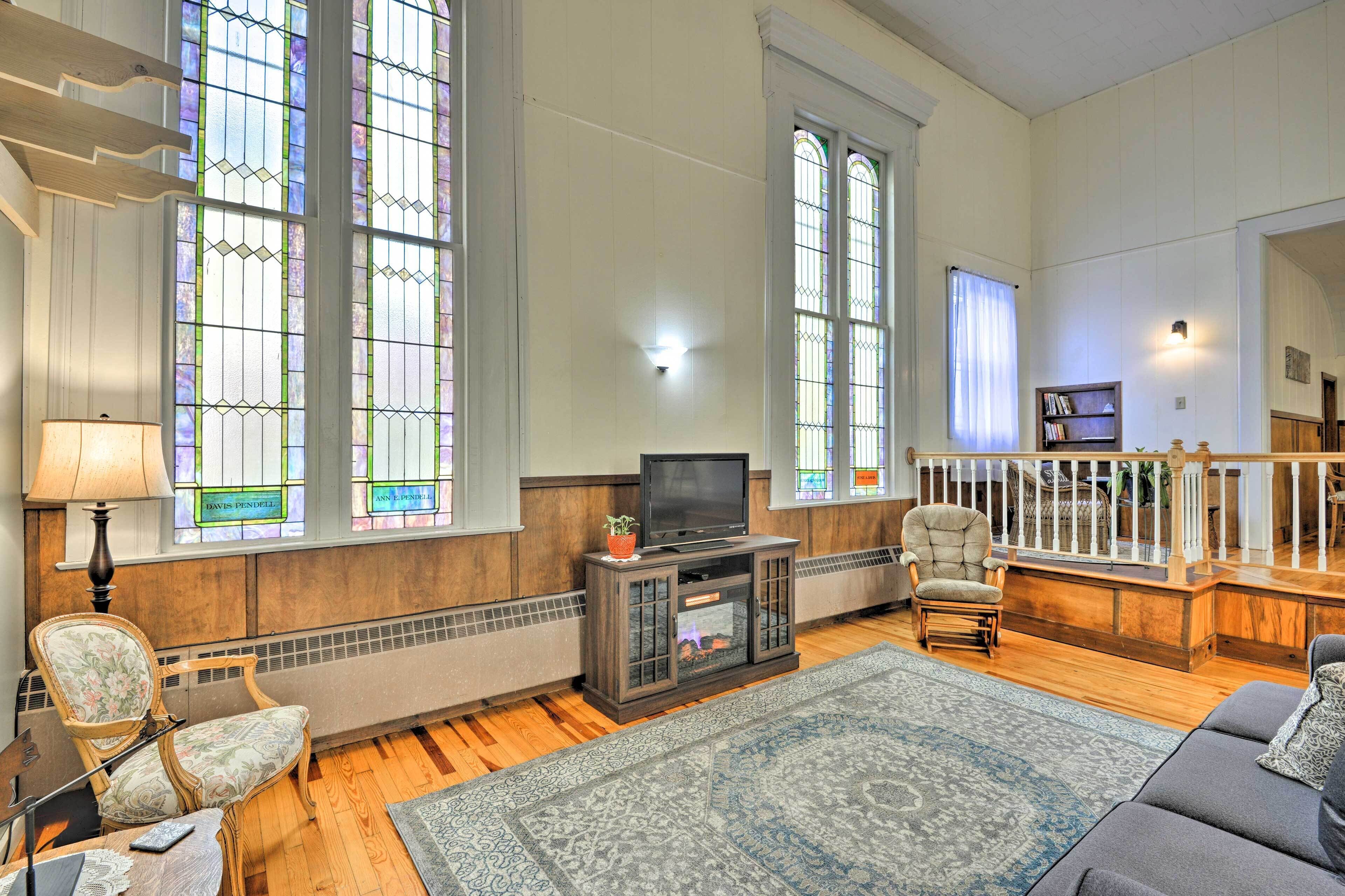 A spacious living room with large windows, a fireplace, a television, and comfortable seating.