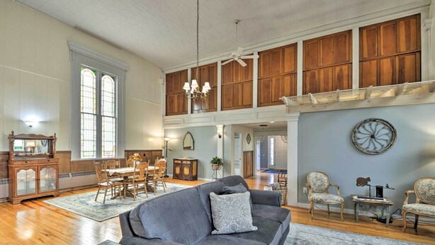 A spacious living room with a high ceiling, wooden paneling, a dining area, and a large window. - Lisle Apt: Fireplace & Stained Glass Windows! (Lisle)
