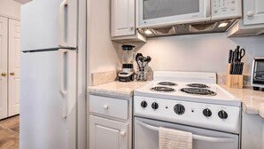 Una cocina con armarios blancos, microondas integrado, estufa y refrigerador.