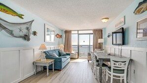 Un salon avec un canapé, une table à manger avec des chaises, un téléviseur et un balcon avec des rideaux.