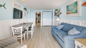 Une pièce comprenant une table à manger, des chaises, un canapé bleu et un tableau encadré accroché au mur.