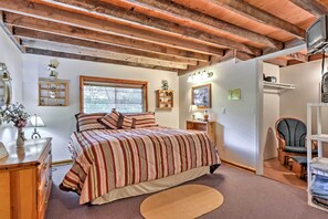 Un dormitorio con techo de madera, una cama con ropa de cama a rayas, una mesita de noche, una lámpara, una silla y un televisor.