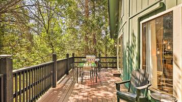 A wooden deck with a table and chairs, surrounded by a black railing and trees.