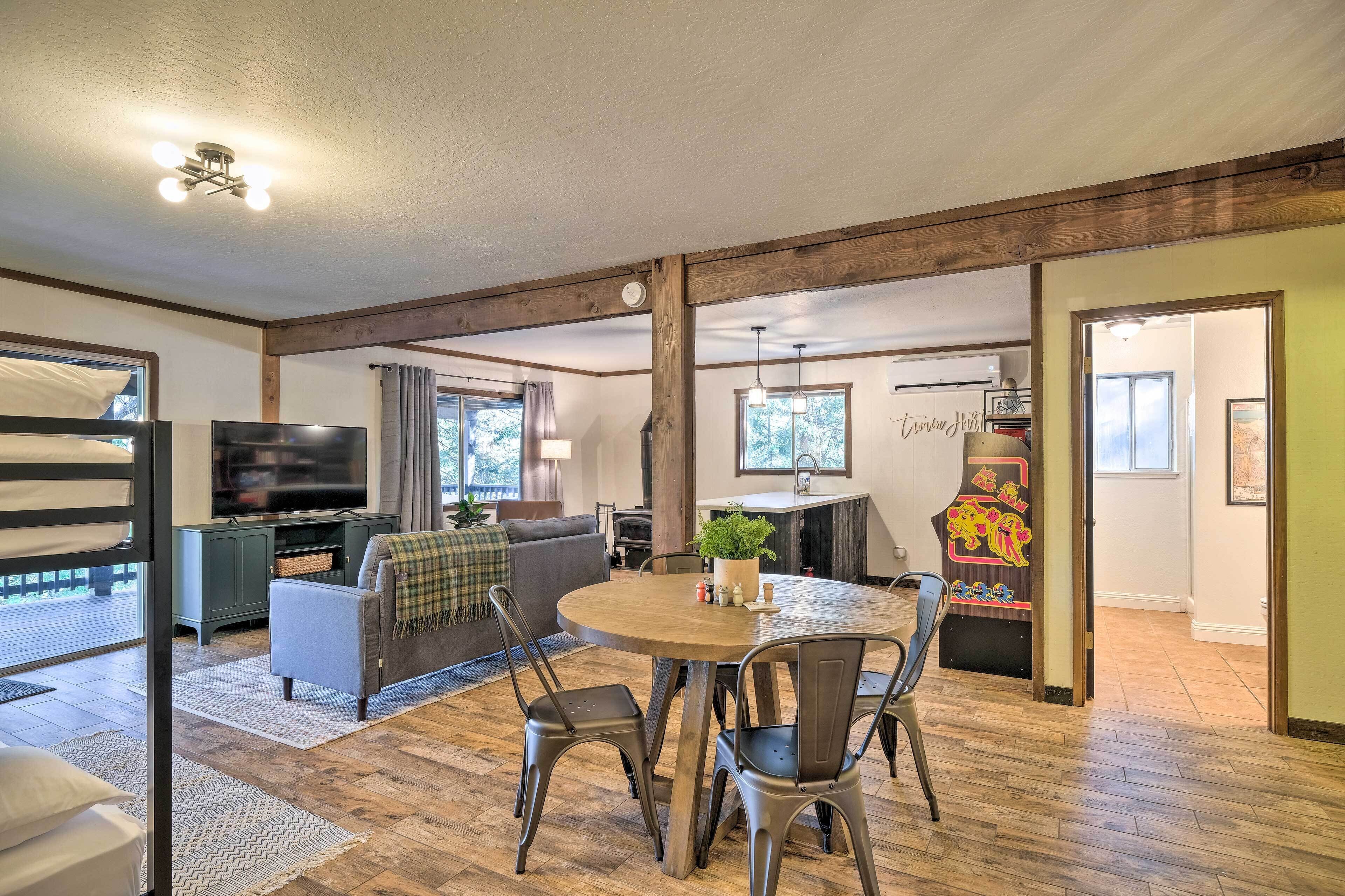 A spacious living area with a round wooden table, comfortable seating, a television, and a kitchen area with a grill.