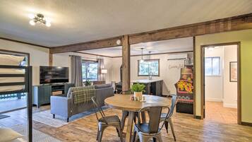 A spacious living area with a round wooden table, comfortable seating, a television, and a kitchen area with a grill.