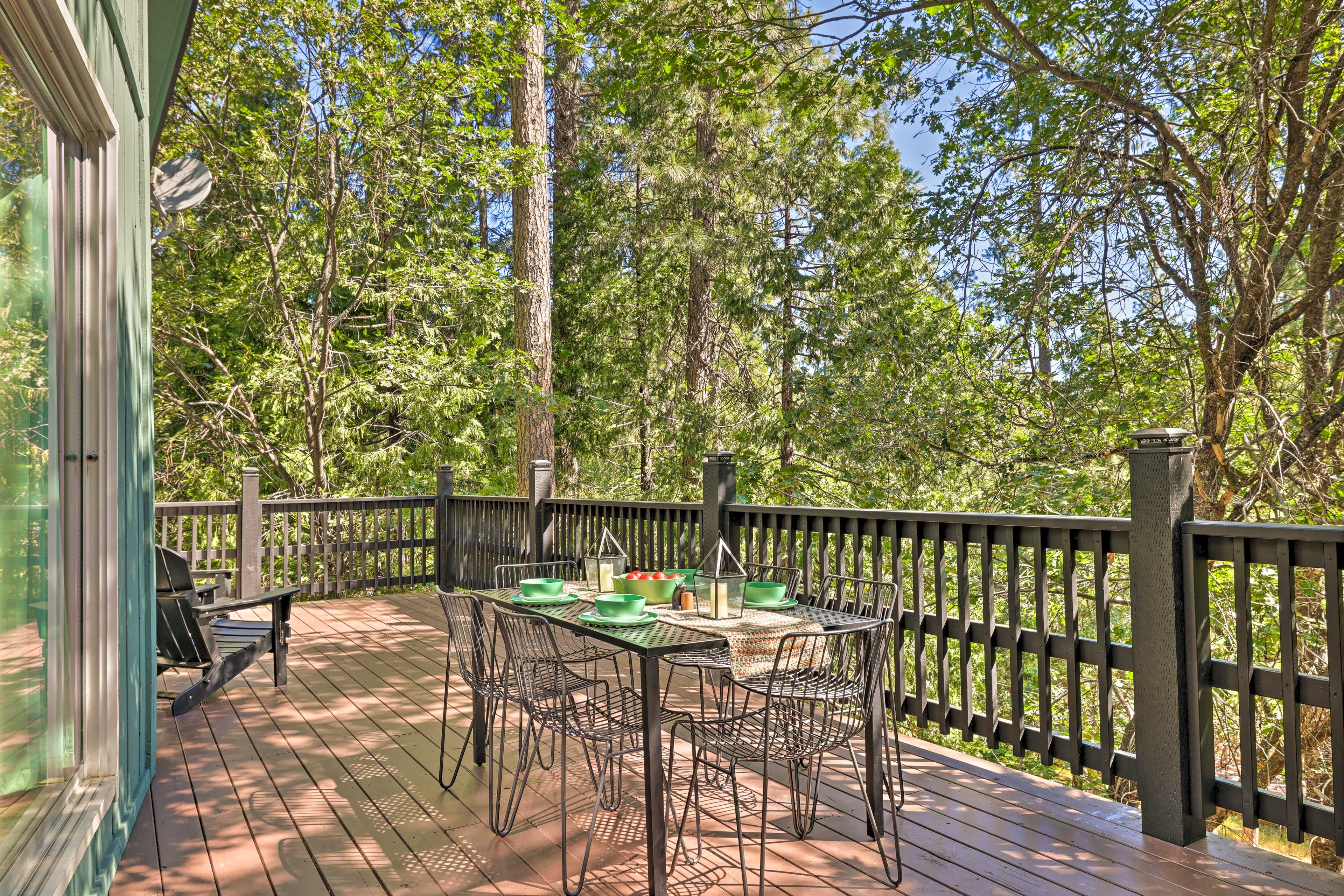 A wooden deck with a table and chairs, surrounded by a wooden railing and trees.