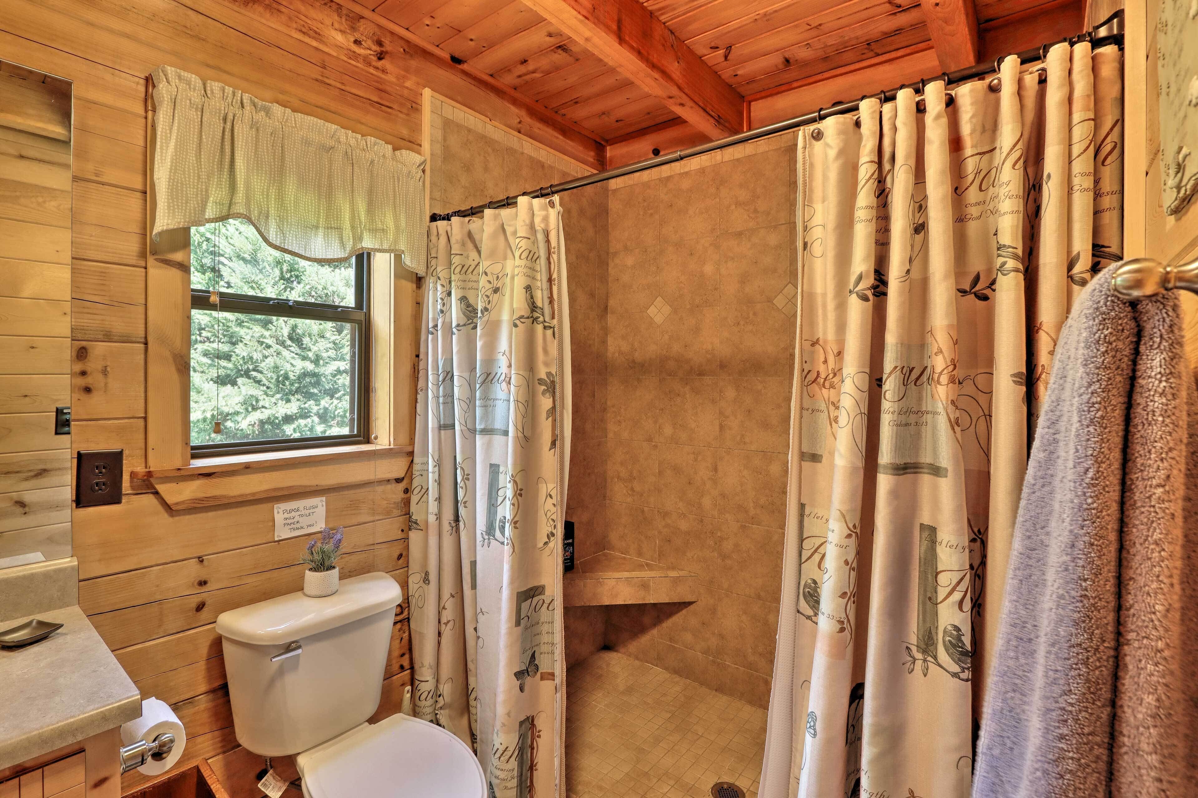 A wooden cabin bathroom with a shower curtain, toilet, and window.