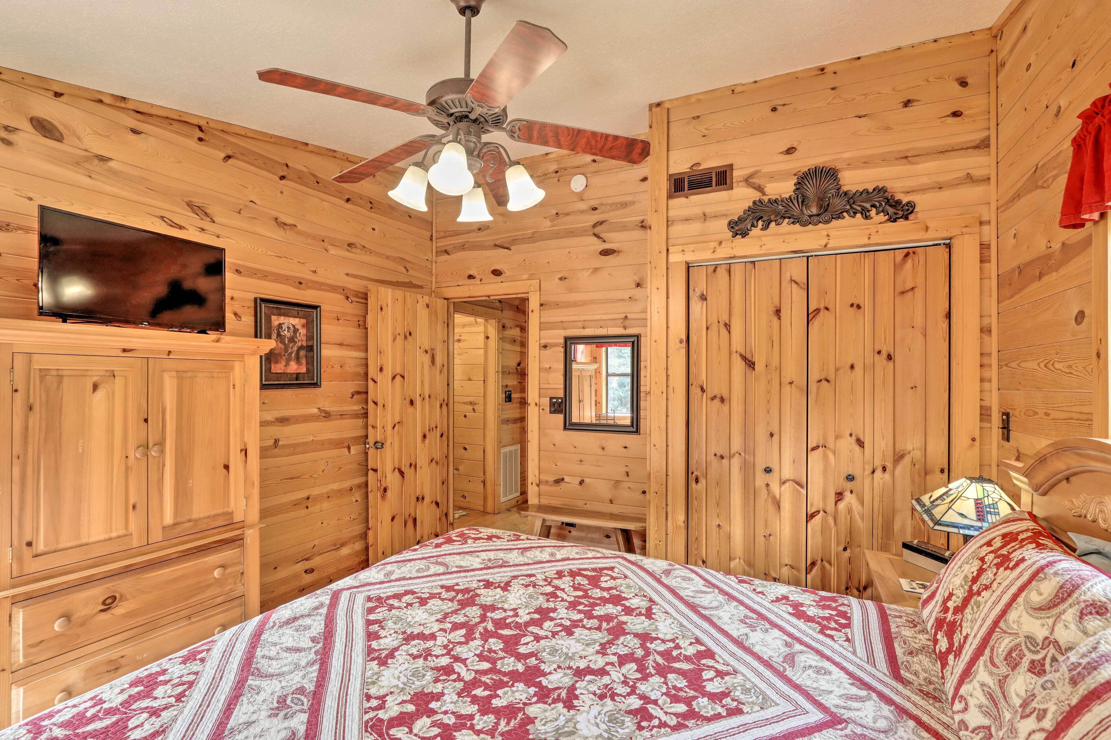 Une chambre aux murs lambrissés, comprenant un lit, un ventilateur de plafond, une télévision et une commode.