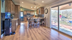 A spacious kitchen with wooden cabinets, a large island with bar stools, and a view of the backyard through glass doors. - Private Dock, Waterfront Views! Sunrise Beach Home (Sunrise Beach)
