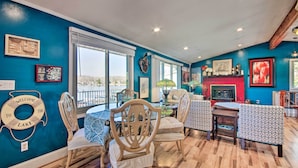 A dining area with a view of the lake, wooden chairs, a table with a blue tablecloth, and a red fireplace. - Private Dock, Waterfront Views! Sunrise Beach Home (Sunrise Beach)