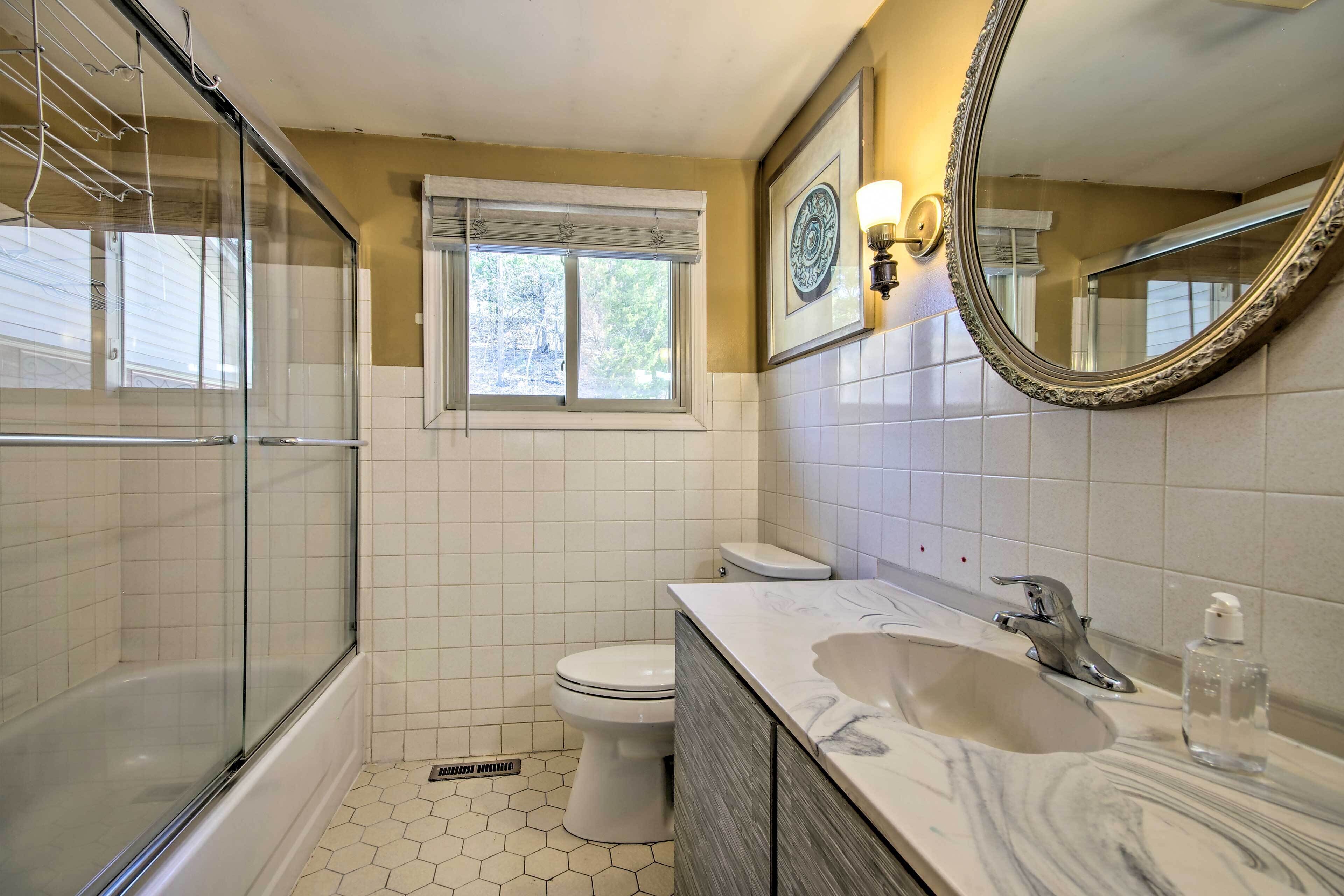 Ein Badezimmer mit Duschkabine aus Glas, Toilette, Waschbecken mit Marmorplatte und Spiegel mit Zierrahmen.