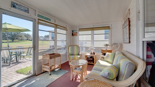 A sunlit room with wicker furniture, a view of a golf course, and a sign reading "GOLFERS PLACE". - Lady Lake House w/ Lanai & Community Pool! (Lady Lake)