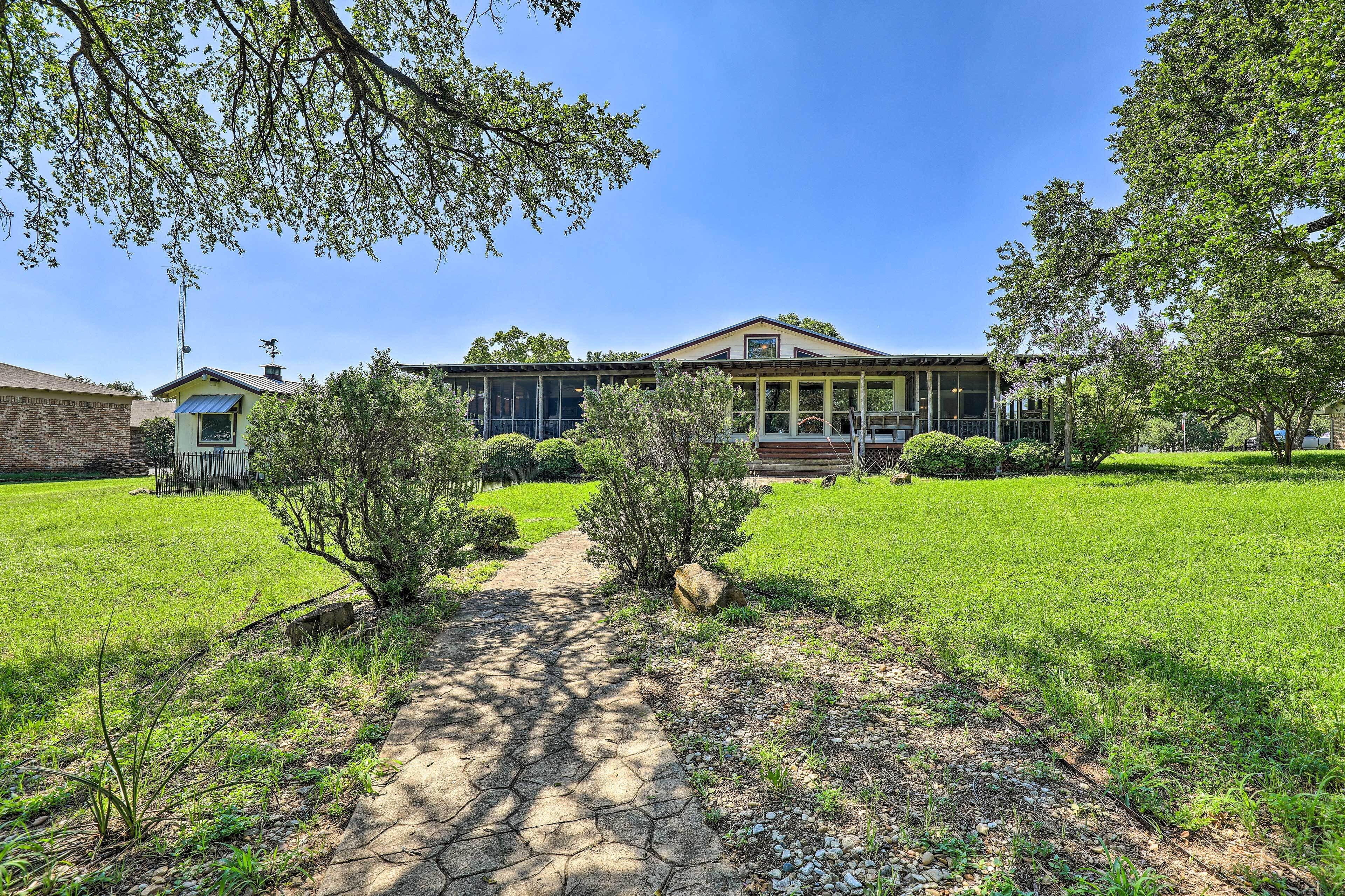 A house with a paved driveway leading to a front door, surrounded by a well-maintained lawn and trees.