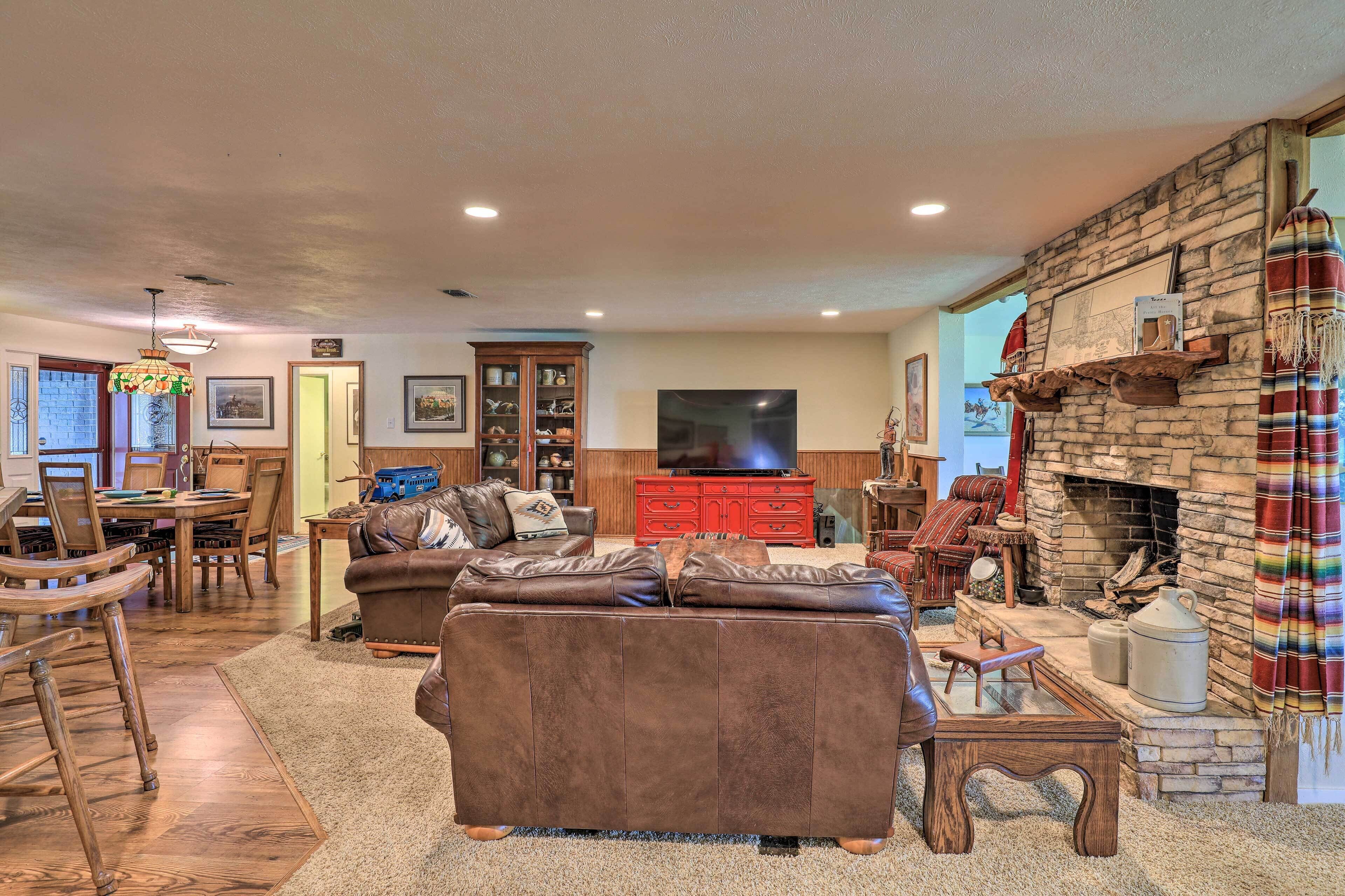 A spacious living room with a stone fireplace, leather sofa, wooden dining table, and a television.