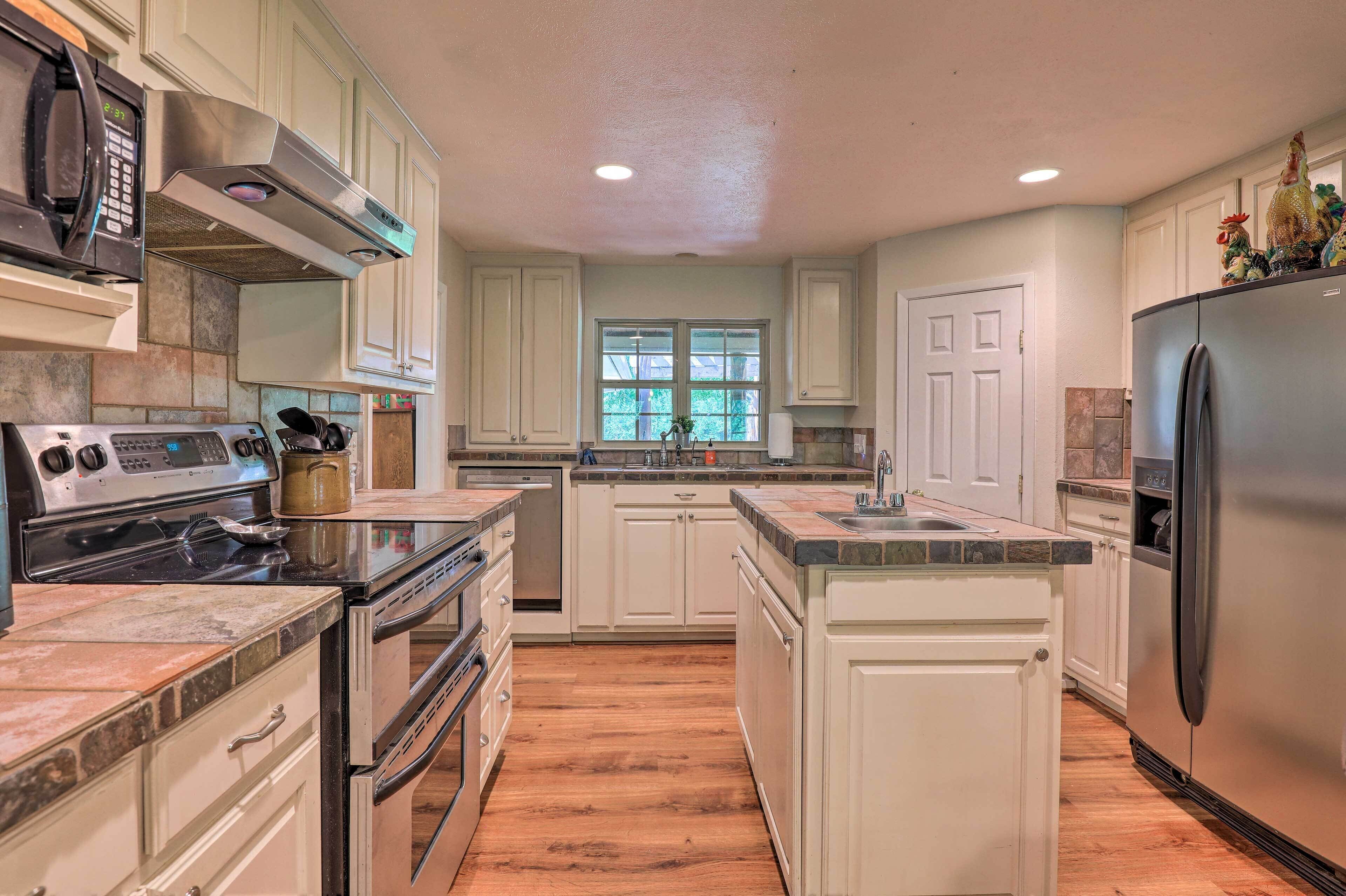 A kitchen with white cabinets, a stainless steel refrigerator, a stove, and a window with a view of greenery.