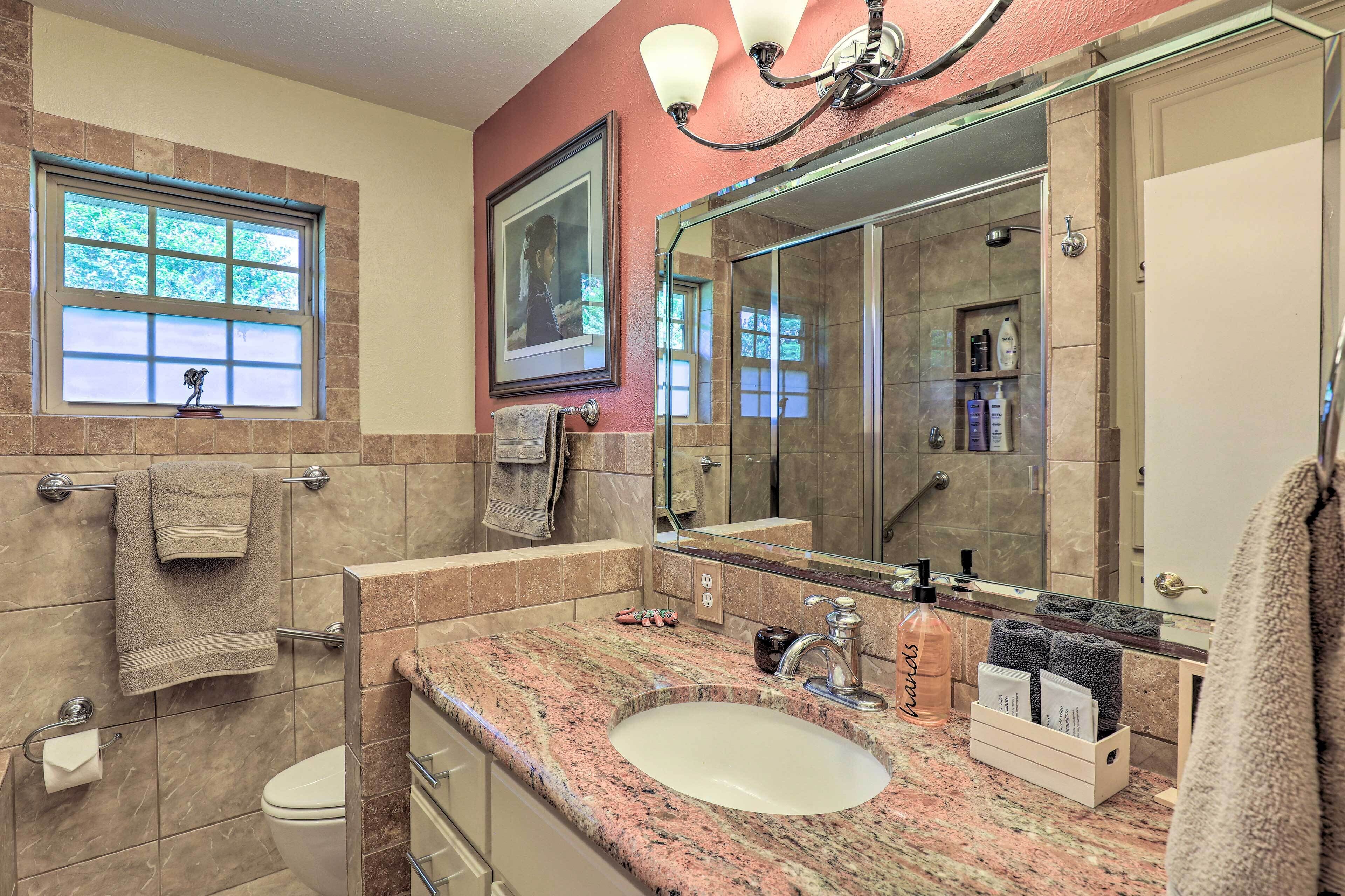 Une salle de bain avec un lavabo en marbre, un grand miroir, une douche et une fenêtre donnant sur la verdure.