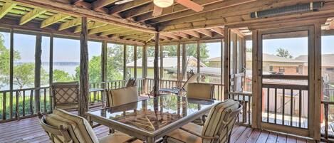 A covered outdoor deck with a glass table and chairs, wooden beams, and a ceiling fan.