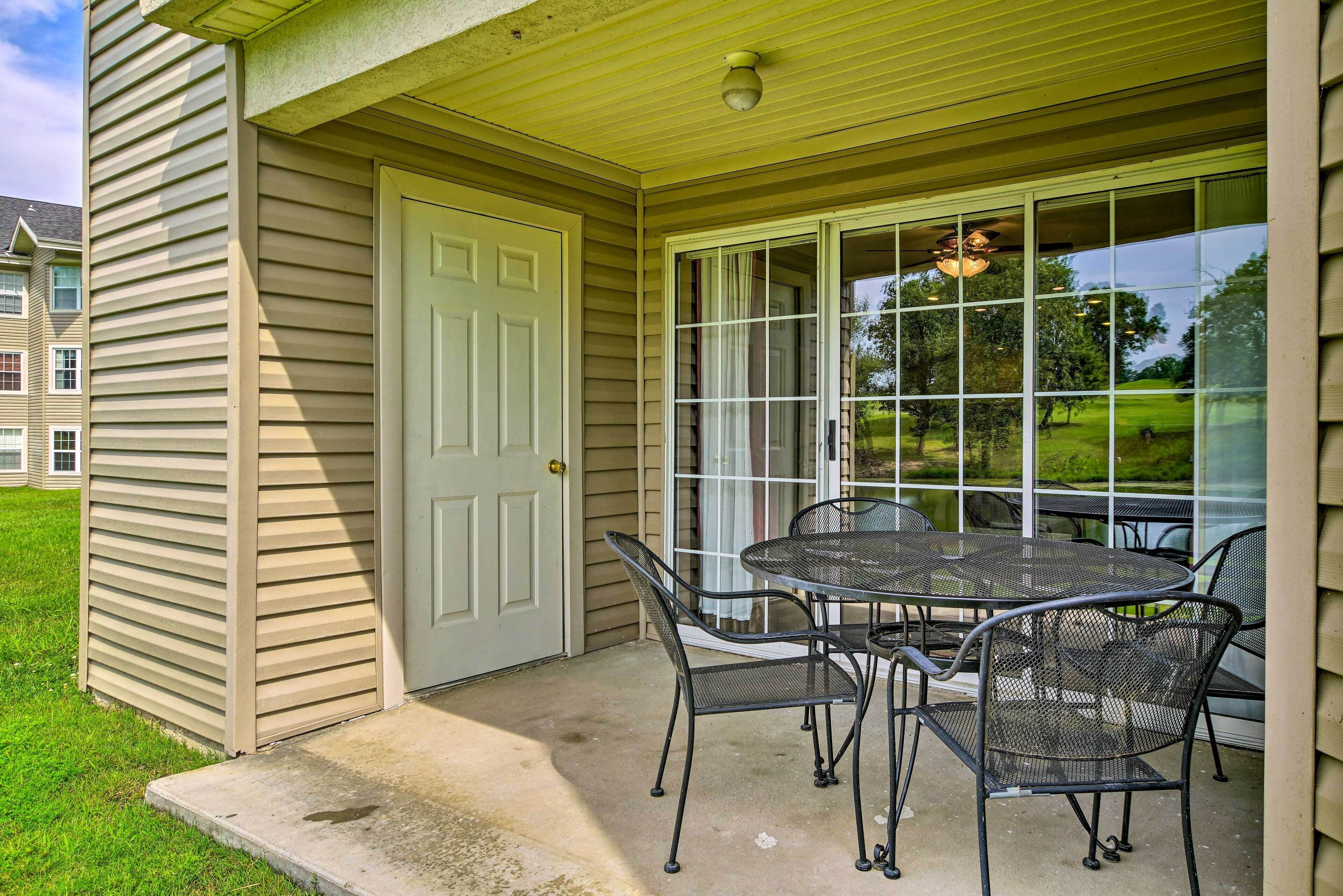 A covered patio with a table and chairs, a door, and a view of a green landscape.