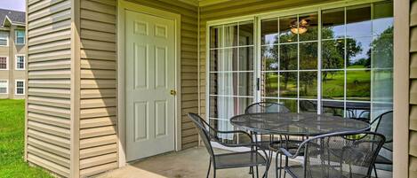 A covered patio with a table and chairs, a door, and a view of a green landscape.