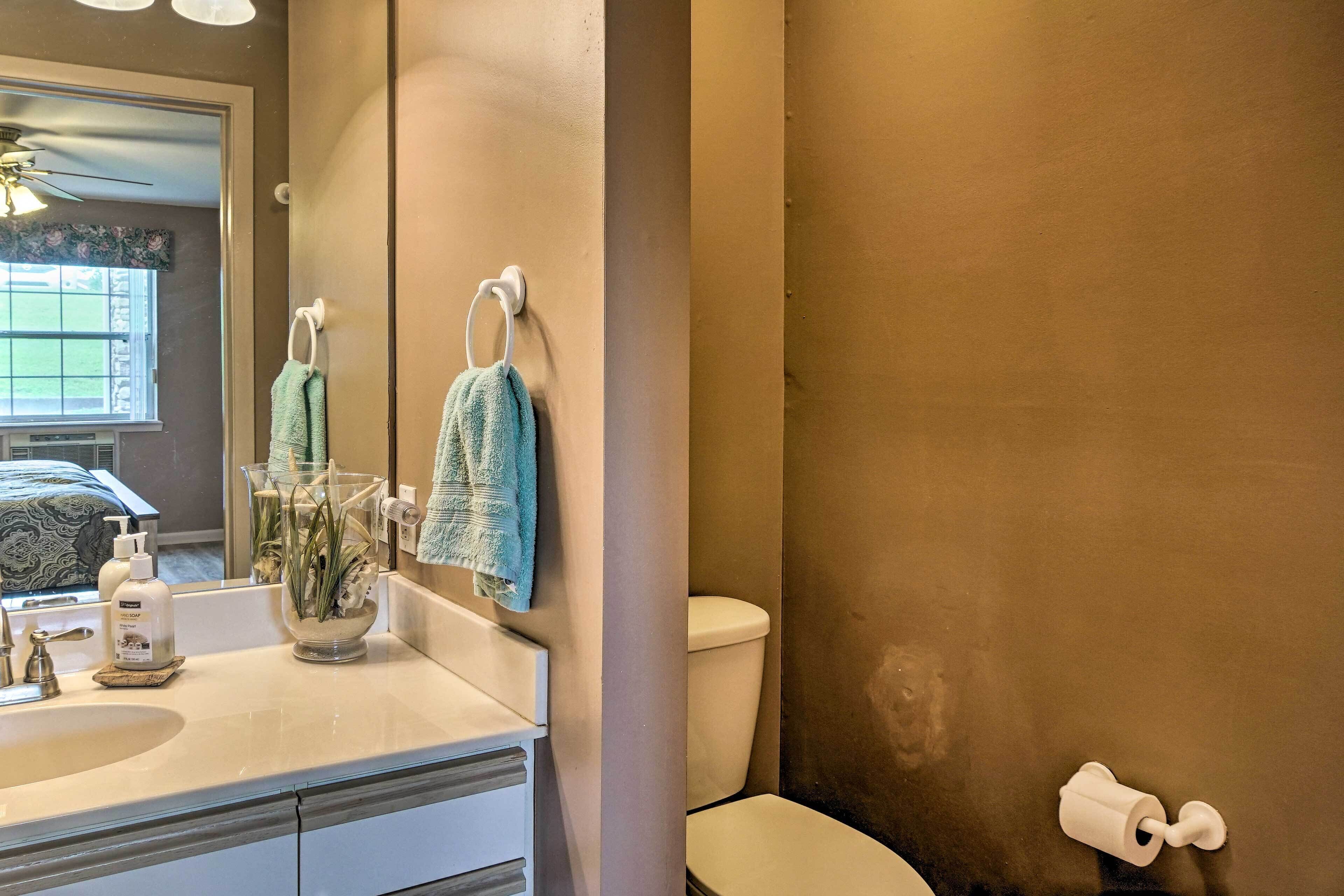 A bathroom with a toilet, sink, and a mirror. There are towels hanging on the wall and a bottle of soap on the counter.