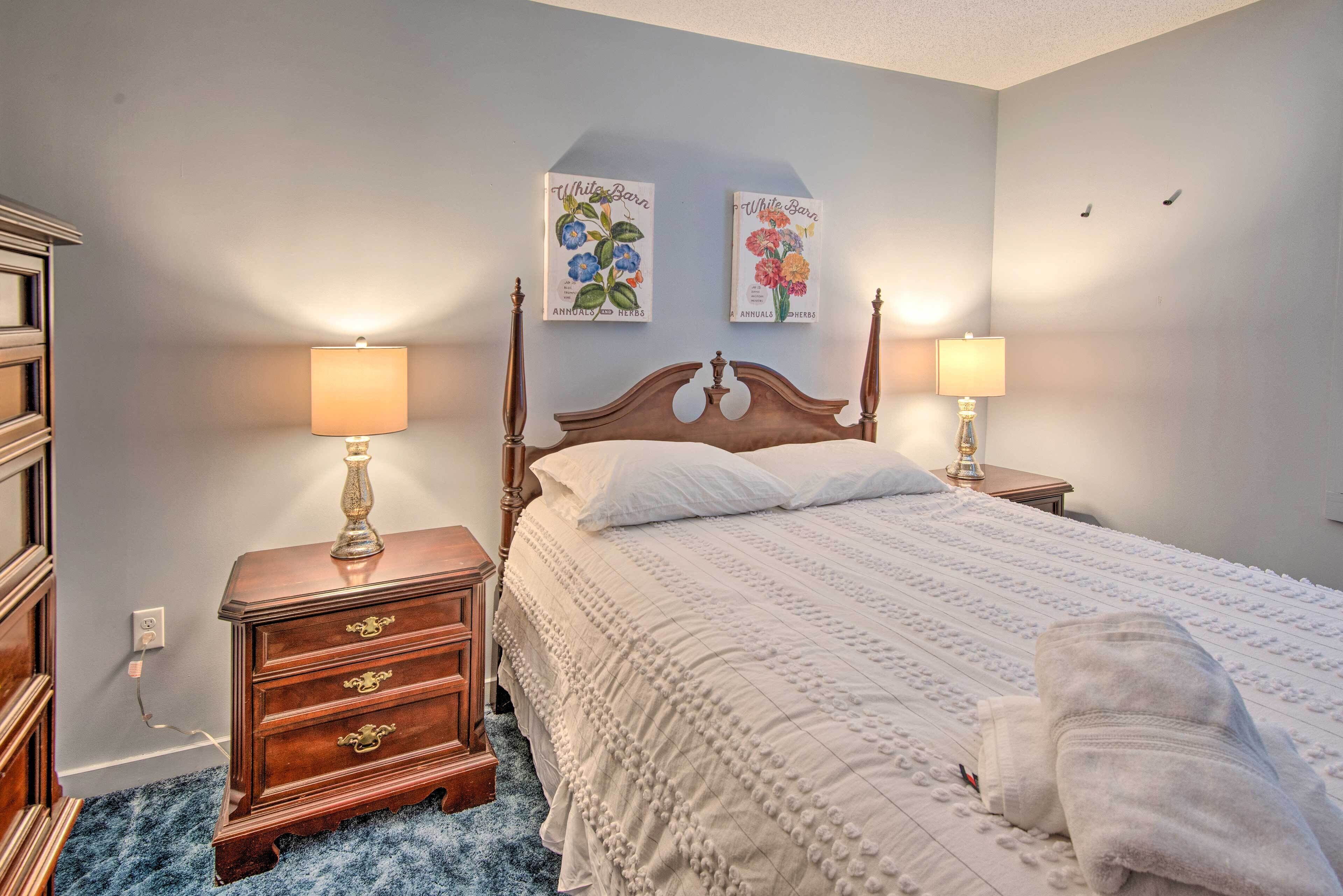 Un dormitorio con una cama de madera, dos mesitas de noche con lámparas, un aparador y dos cuadros colgados en la pared.