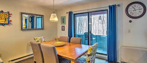 Een eetruimte met een houten tafel, vier stoelen, een hanglamp, een wandklok en een raam met gordijnen.