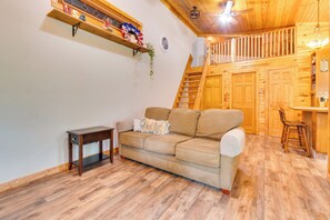 Un accogliente soggiorno con pavimento in legno, un divano beige, un tavolino e una scala che conduce a una zona mansardata.