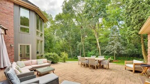 A patio area with wicker furniture, a brick wall, and a view of a forest. - Spacious & Secluded Madison Home Near Dtwn! (Madison)