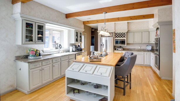 A modern kitchen with white cabinetry, wooden beams, and a central island with bar stools. - Spacious & Secluded Madison Home Near Dtwn! (Madison)