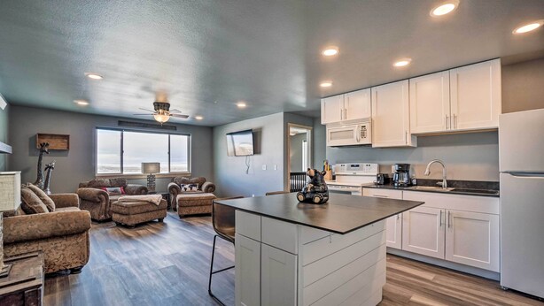 Una cocina moderna con armarios blancos, una isla central y una zona de comedor con sofás y una mesa de centro.